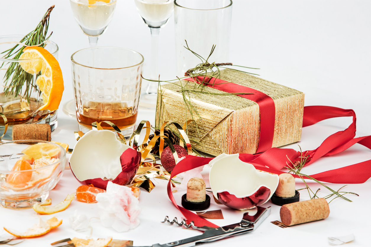 Leere und halbleere Gläser, verpackte Weihnachtsgeschenke und zerbrochener Weihnachtsschmuck auf einem weissen Tisch.