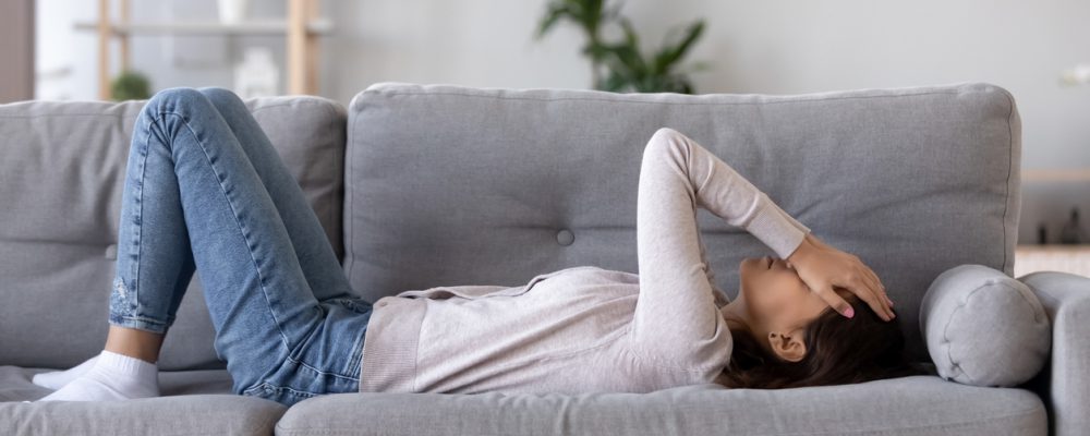Eine junge Frau liegt mit Migräne auf dem Sofa.