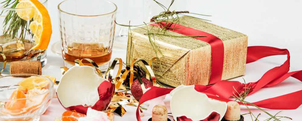 Leere und halbleere Gläser, verpackte Weihnachtsgeschenke und zerbrochener Weihnachtsschmuck auf einem weissen Tisch.