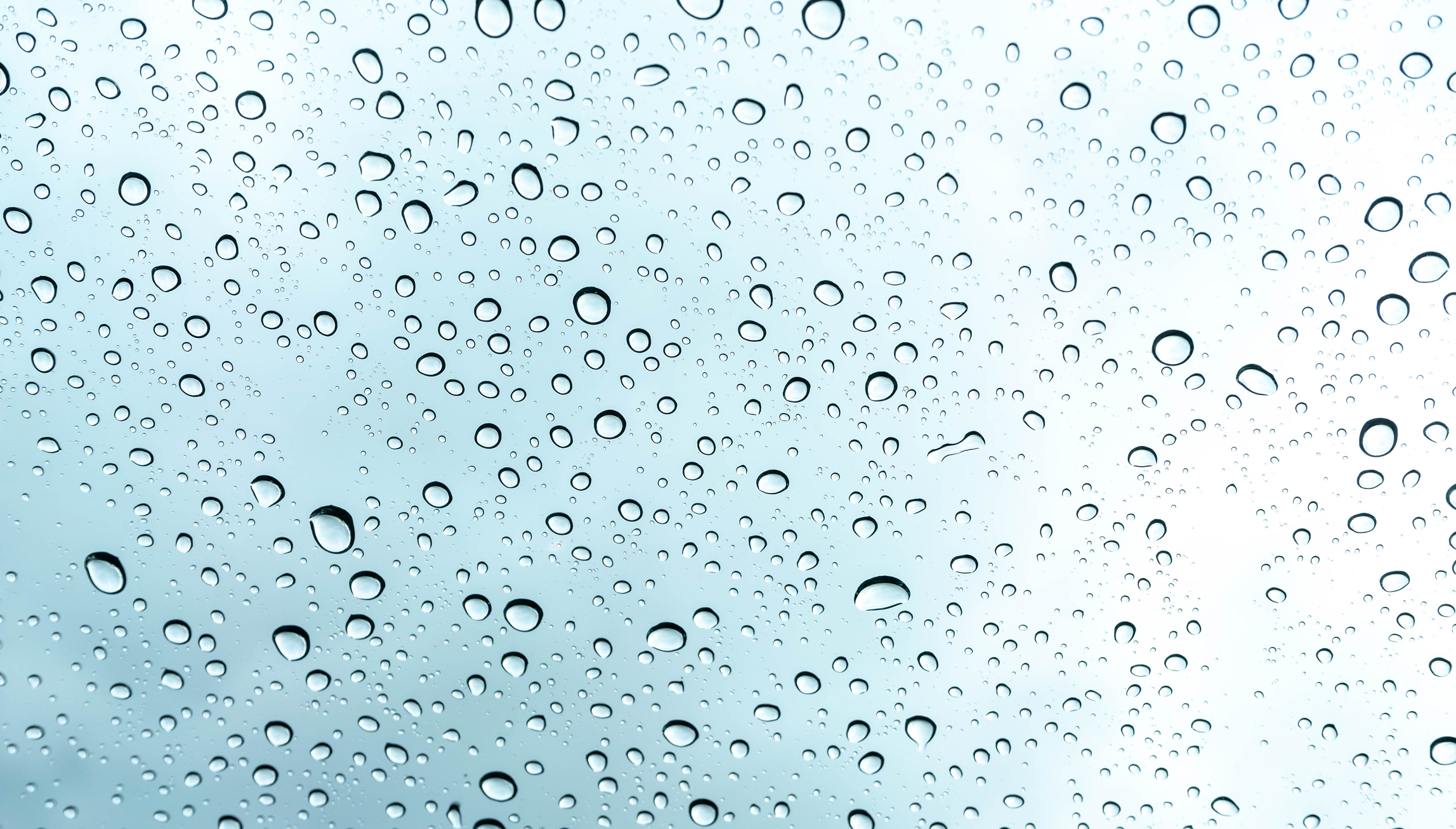 An image of water drops on glass in front of a light blue background.