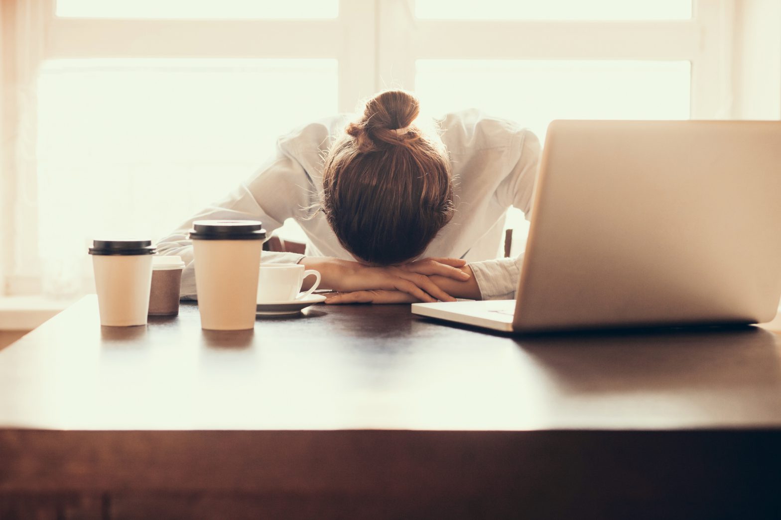 A woman sitting at an office desk with her head in her hands, having a migraine attack