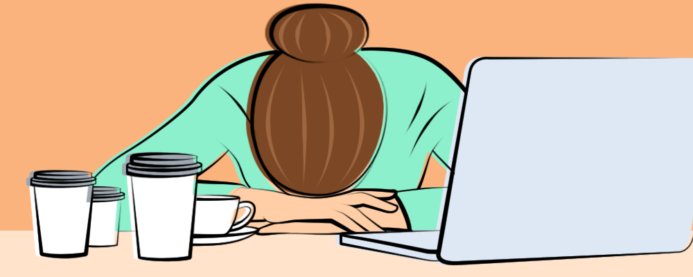 A woman with migraine sitting at a desk with her head in her hands.