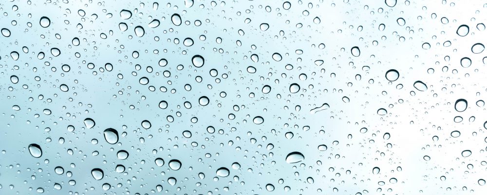 An image of water drops on glass in front of a light blue background.